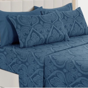 May include: A blue paisley patterned bed sheet set. The set includes a fitted sheet, flat sheet, and pillowcases. The paisley design is a lighter shade of blue against a darker blue background. The bed is made up with the sheets and pillowcases.