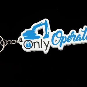 May include: A white keychain featuring a blue excavator silhouette, a blue padlock icon, and the text Only Operators in blue script lettering. The design is attached to a standard silver-colored metal split ring by a short metal chain link.