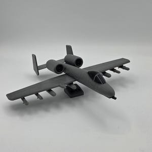 May include: A gray model airplane with two engines, wings, and a cockpit. The model has detailed features, including missiles under the wings. The airplane is a replica of a military aircraft.