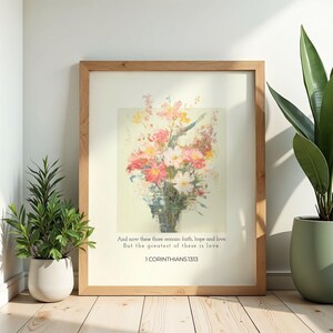 Puede incluir: Una impresión floral enmarcada con un ramo de flores rosas, amarillas y blancas en un jarrón. La obra de arte tiene un fondo claro e incluye el texto "And now these three remain faith, hope and love. But the greatest of these is love. 1 CORINTHIANS 13:13."