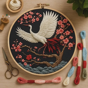 Puede incluir: Obra de arte bordada que presenta una grulla blanca con plumas de cola rojas y un cerezo en flor sobre un fondo negro. El bordado está en un bastidor de madera, con suministros de bordado adicionales.