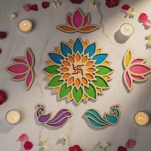 Könnte beinhalten: Eine Sammlung farbenfroher Holzdekorationen, darunter ein großes Mandala mit einem zentralen Symbol, Lotusblumen und Pfauenformen. Die Teile sind mit Kerzen, Blütenblättern und kleinen weißen Blumen angeordnet.