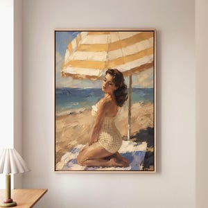 May include: An oil painting in a wooden frame depicting a person kneeling on a beach towel under a yellow and white striped umbrella. The person wears a light-colored patterned swimsuit. The scene features a sandy beach and blue ocean waves.