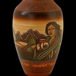 May include: A hand-painted ceramic vase with a Native American design. The vase features a woman holding a pot, mountains, and geometric patterns in shades of brown, tan, and blue. The vase is approximately 12 inches tall.