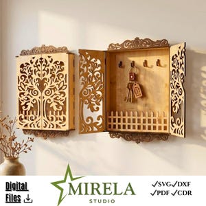 Op de afbeelding: Houten sleutelhouder met een boomontwerp, met lasergesneden details. De sleutelhouder heeft een scharnierende deur en een klein hekwerk aan de onderkant. De sleutelhouder is aan een muur bevestigd en bevat een set sleutels.