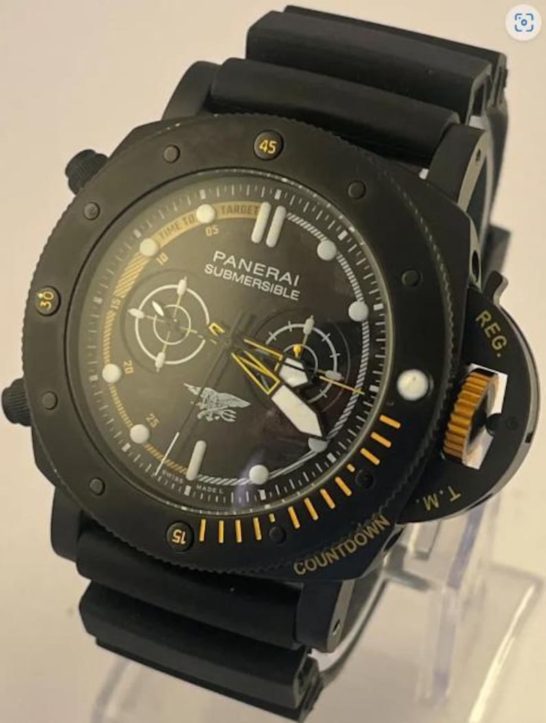 May include: A black Panerai Submersible watch with a black rubber strap. The dial features white hour markers, yellow accents, two sub-dials, and a Navy SEALs trident emblem. The bezel includes yellow numerals and the text COUNTDOWN and REG. T.M.