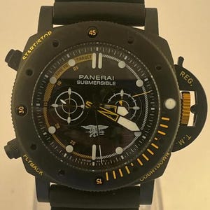 May include: A black Panerai Submersible watch with a rubber strap. The dial features yellow accents, white luminous markers, two sub-dials, and a Navy SEALs trident emblem. The bezel includes text reading START/STOP, FLYBACK, REG. T.M., and COUNTDOWN.