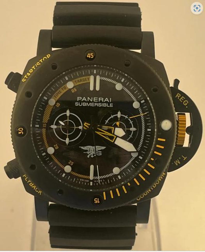 May include: A black Panerai Submersible watch with a rubber strap. The dial features yellow accents, white luminous markers, two sub-dials, and a Navy SEALs trident emblem. The bezel includes text reading START/STOP, FLYBACK, REG. T.M., and COUNTDOWN.