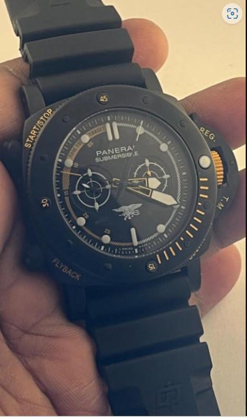 May include: A black Panerai Submersible watch with a black rubber strap, a round black dial featuring gold-toned hands, markers, and text, including the word START/STOP, FLYBACK, and REG. The dial displays a central emblem and sub-dials.