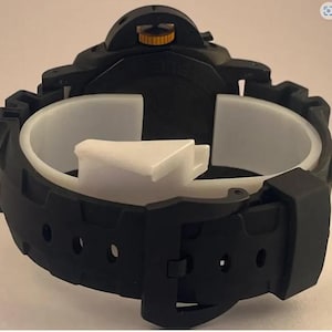 May include: A black wristwatch featuring a matte finish, a thick rubber strap with a buckle closure, and a prominent crown guard mechanism. The watch crown is accented with a metallic gold color, providing a contrast against the black casing.