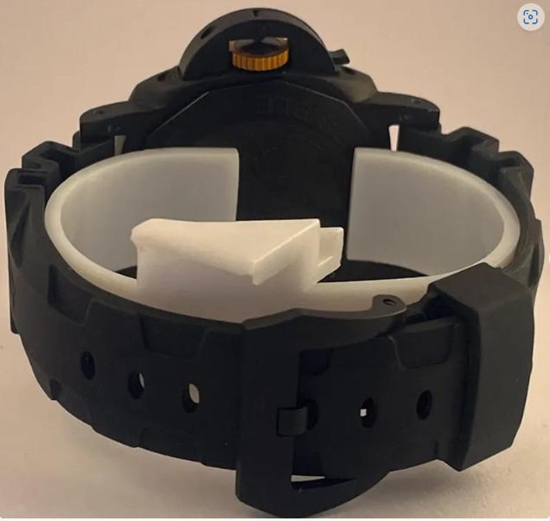 May include: A black wristwatch featuring a matte finish, a thick rubber strap with a buckle closure, and a prominent crown guard mechanism. The watch crown is accented with a metallic gold color, providing a contrast against the black casing.