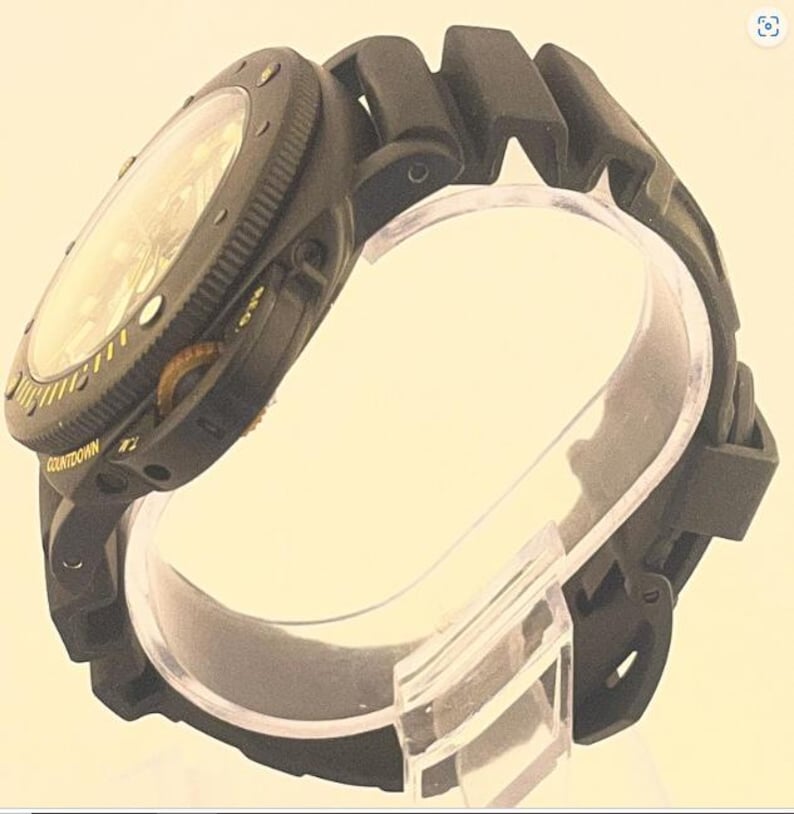 May include: A black wristwatch featuring a textured rubber strap and a round case with a rotating bezel. The bezel displays the word COUNTDOWN in yellow lettering. The watch face is protected by a clear crystal, and the side of the case includes a crown.