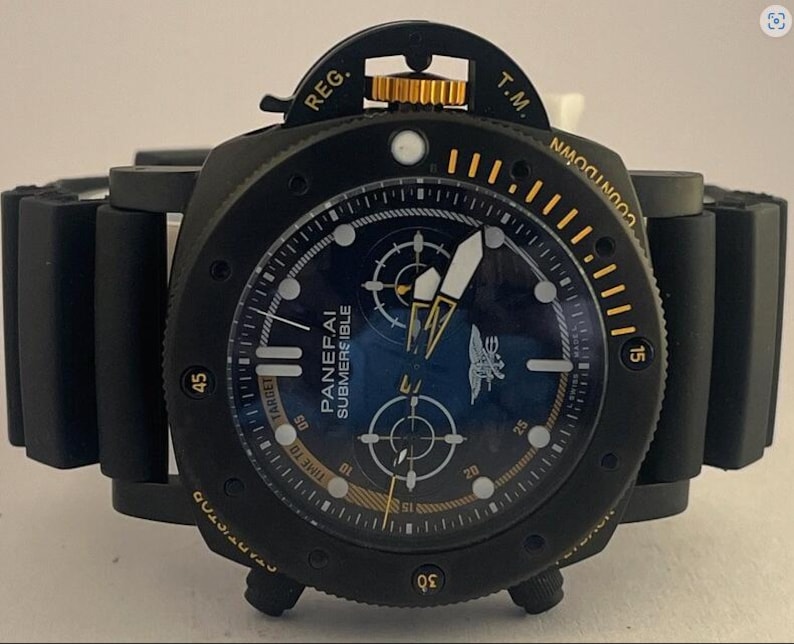 May include: A black Panerai Submersible watch with a dark blue dial, featuring a gold-colored crown, luminous hands, and a black rubber strap. The bezel includes yellow markers and the text COUNTDOWN, while the dial displays the Panerai logo.