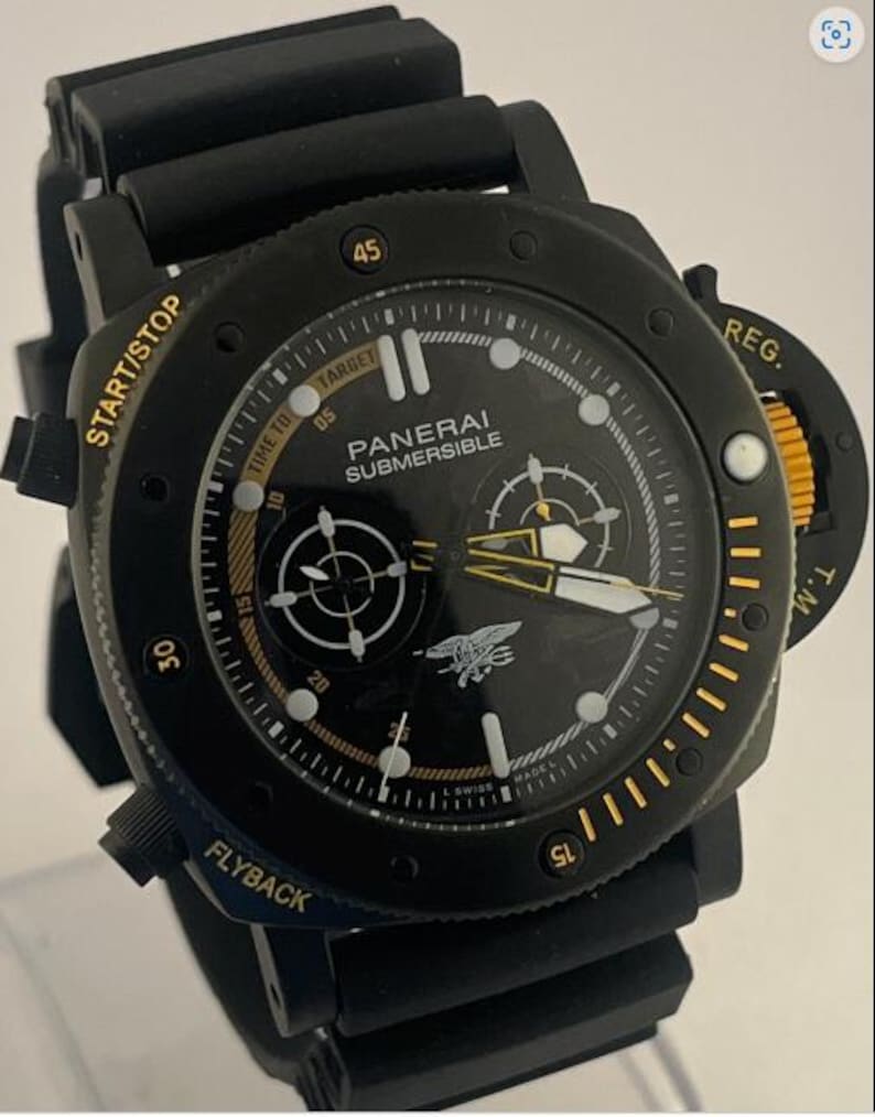 May include: A black Panerai Submersible watch with a black rubber strap. The dial features gold-toned text including START/STOP, REG., and FLYBACK, with a central trident emblem. The bezel has gold markers and the dial displays white hour indices.