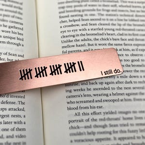May include: A copper-colored metal bookmark with etched tally marks and the phrase "I still do." The bookmark is rectangular and lies on an open book, enhancing the reading experience.