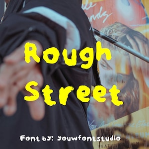May include: The words "Rough Street" in a bright yellow, stylized font are centered in the image. The background is blurred, with a person's arm and part of a black jacket in the foreground. The text "Font by: youwfontstudio" is at the bottom.