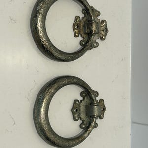 May include: Two circular metal ring pulls with a weathered, dark silver-toned finish. Each pull features a decorative mounting plate with two screw holes. The bottom ring displays the embossed text "WELCH" and "1007" on its surface.
