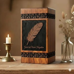 Peut inclure: Urne funéraire en bois avec une plume sculptée et l'inscription "Gone but Never Forgotten". Le coffret rectangulaire présente des motifs floraux et un panneau texturé foncé. Une bougie allumée et un vase de fleurs séchées sont visibles.