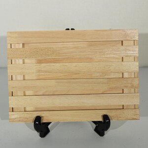 May include: A rectangular light-colored wooden board constructed from several horizontal slats joined together. The board features a natural wood grain pattern with visible finger joints on the edges, showcasing a light tan color throughout the surface.