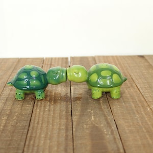 May include: A white ceramic mug with a black handle and the text "But First, Coffee" in a black, handwritten-style font. The mug is on a white surface.