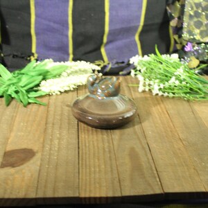 May include: A brown ceramic insulator with a blue and brown top sits on a wooden surface. Green and white artificial flowers are arranged around the insulator. The background includes patterned fabric.