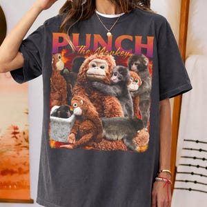 以下が含まれることがあります： 様々なポーズの猿のグラフィックが特徴の濃いグレーのTシャツ。「PUNCH The Monkey」の文字がオレンジと紫でプリントされています。ゆったりとしたフィット感のシャツです。