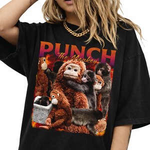 May include: Black t-shirt featuring a graphic of several monkeys with the text "PUNCH The Monkey" in orange and purple. The monkeys are various shades of brown and gray, with a fiery background.