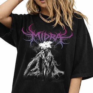 May include: Black t-shirt featuring the word "MIDRA" in a stylized, purple and pink font above a ghostly figure. The figure is white and appears to be wearing a cloak. The shirt has a vintage, worn look.
