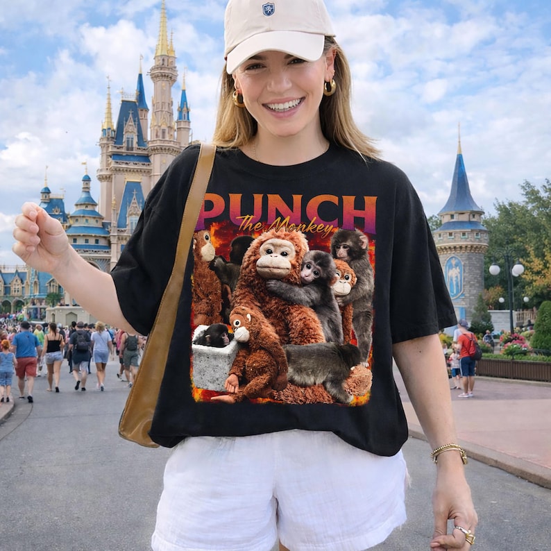 May include: Black t-shirt with a graphic of several monkeys and the text "PUNCH The Monkey" in orange and purple. The monkeys are various shades of brown and gray. The shirt is worn by a person.