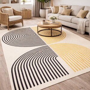 Könnte beinhalten: Ein cremefarbener Teppich mit geometrischem Design. Der Teppich hat geschwungene schwarze und gelbe Linien, die ein modernes, abstraktes Muster bilden. Der Teppich ist rechteckig und liegt auf einem Holzboden.