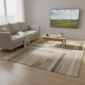Könnte beinhalten: Ein rechteckiger Teppich mit geometrischem Muster in Beige-, Tan- und Brauntönen. Der Teppich liegt auf einem hellen Holzboden in einem Wohnzimmer. Ein graues Sofa und ein Holztisch sind ebenfalls zu sehen.
