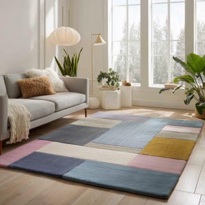 Könnte beinhalten: Ein rechteckiger Teppich mit einem Patchwork-Design in Blau-, Rosa-, Grau- und Gelbtönen. Der Teppich liegt auf einem Holzboden in einem Wohnzimmer. Der Raum verfügt außerdem über ein graues Sofa und große Fenster.