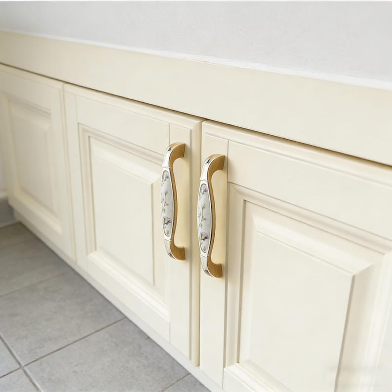 Peut inclure: Portes d'armoires cr&egrave;me avec des poign&eacute;es d&eacute;coratives dor&eacute;es et florales. Les poign&eacute;es ont un design incurv&eacute; et sont mont&eacute;es sur les portes d'armoires blanc cass&eacute;. Les portes d'armoires font partie d'un plus grand &eacute;l&eacute;ment int&eacute;gr&eacute;.