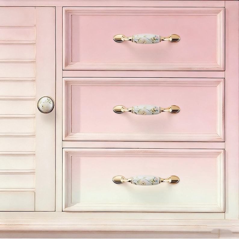 Peut inclure: Un meuble rose clair avec trois tiroirs et une porte lat&eacute;rale. Les tiroirs ont des poign&eacute;es dor&eacute;es avec un motif floral. La porte de l'armoire a un bouton rond avec un motif floral assorti. L'armoire est peinte dans une palette de couleurs pastel douces.