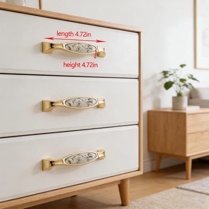 Peut inclure: Poign&eacute;es de tiroir dor&eacute;es avec inserts en c&eacute;ramique florale. Chaque poign&eacute;e mesure 12 cm de long et de haut. Mont&eacute;es sur des tiroirs blancs avec un cadre en bois clair, elles offrent un design classique et &eacute;l&eacute;gant pour les meubles.