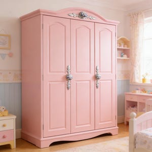 以下が含まれることがあります： ピンク色の木製ワードローブ、3つのドア付き。ワードローブには、青と白のアクセントが付いた装飾的なシルバーのハンドルが付いています。ワードローブの上部には、装飾的なシルバーとブルーのアクセントがあります。ワードローブは寝室にあります。