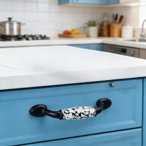 以下が含まれることがあります： 青いキッチンキャビネットのクローズアップ。黒い取っ手が付いています。取っ手は白と黒のモザイク模様です。キャビネットは白いカウンタートップのあるキッチンアイランドの一部です。