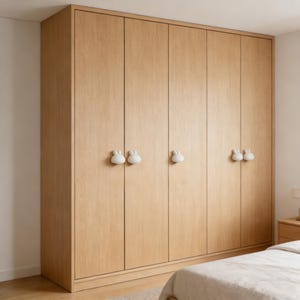 May include: A large, light-colored wooden wardrobe with six doors. Each door has a pair of white, bunny-shaped handles. The wardrobe is a light brown color and is set against a white wall.
