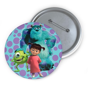 Könnte beinhalten: Ein runder Button mit Figuren aus dem Animationsfilm "Die Monster AG". Der Button zeigt Mike Glotzkowski, Boo und Sulley vor einem hellblauen Hintergrund mit lila Punkten. Der Button hat eine silberne Nadelrückseite.