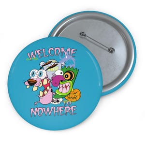 以下が含まれることがあります： ピンク色の「WELCOME to NOWHERE」という文字が入った、丸い水色のボタン。ピンクの犬、緑のモンスター、カボチャなど、漫画のキャラクターが描かれています。ボタンの裏側は銀色です。