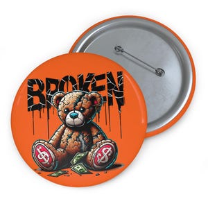 Könnte beinhalten: Orangener Button mit einer Grafik eines Teddybären mit Dollarzeichen auf den Füßen und dem Wort "BROKEN" in schwarzen, tropfenden Buchstaben. Der Bär ist braun, hat blaue Augen und sitzt auf einem Haufen Geld.