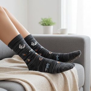 May include: Dark gray socks with a repeating pattern of small, whimsical illustrations. The design includes images of animals, carrots, and other decorative elements. The socks are worn on a person's legs, resting on a sofa.