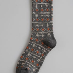 May include: A charcoal gray knit sock featuring a repeating pattern of small orange diamonds and light beige star-like shapes. The sock has a ribbed cuff at the top, a reinforced heel, and a rounded toe section, all in a consistent dark gray.