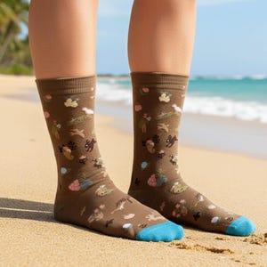 May include: A pair of brown socks with a whimsical pattern of various animals and plants. The socks have blue toes and are worn on a sandy beach. The socks are a fun and colorful accessory.