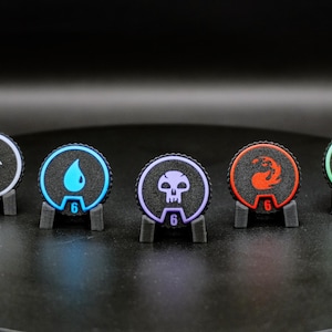 May include: Five circular game counters with textured black surfaces, each featuring a distinct colored icon and number. The icons include a white sun, blue water drop, purple skull, red flame, and green tree, with numbers 11, 6, 6, 6, and 20.