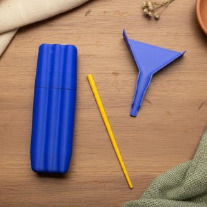 May include: A blue, ribbed, cylindrical container, a yellow straw, and a blue funnel are arranged on a wooden surface. A small terracotta dish with a wooden cannabis leaf is in the background.