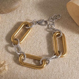 May include: A chain link bracelet featuring alternating large matte gold-tone oval links and smaller silver-tone textured circular links. The bracelet includes a silver-tone lobster claw clasp and an adjustable extender chain with circular links.