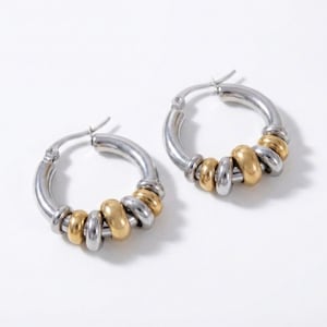 May include: A pair of hoop earrings with a silver-tone base and gold-tone accents. The earrings feature a series of small, round gold beads and silver beads. The earrings are displayed on a white background.