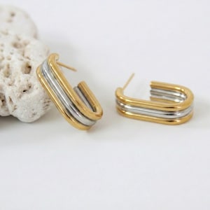 Peut inclure: Boucles d'oreilles créoles dorées et argentées. Chaque boucle d'oreille a une forme rectangulaire avec une couche extérieure dorée et une couche intérieure argentée. Elles sont présentées sur un fond blanc.