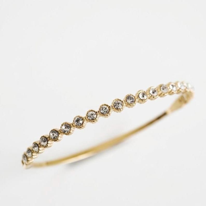 Puede incluir: Un brazalete dorado adornado con una serie de peque&ntilde;as piedras preciosas redondas y transparentes. Las piedras est&aacute;n engastadas en la parte superior del brazalete. Este dise&ntilde;o crea un aspecto refinado y elegante, ideal para cualquier ocasi&oacute;n.